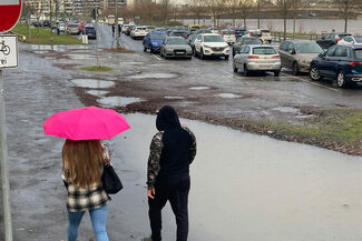 Eine Frau mit Regenschirm und ein Mann gehen über den Mainuferparkplatz in Offenbach.