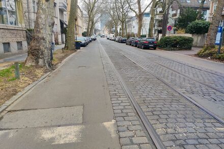 Zu sehen ist eine Straße mit Straßenbahnschienen, links und rechts ist ein Streifen der Straßen betoniert, unter den Schienen liegt aber Kopfsteinpflaster.