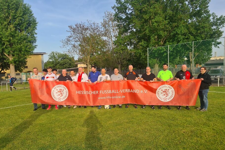 Eine Gruppe von Männern auf einem Fußballfeld, die ein Banner vom Hessischen Fußball-Verband halten.