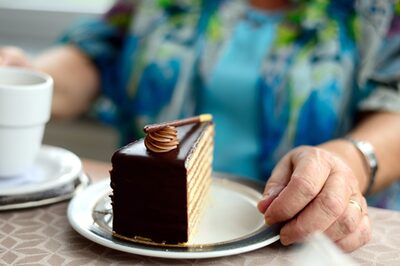 Eine Seniorin sitzt mit Kaffee und Kuchen an einem Tisch.