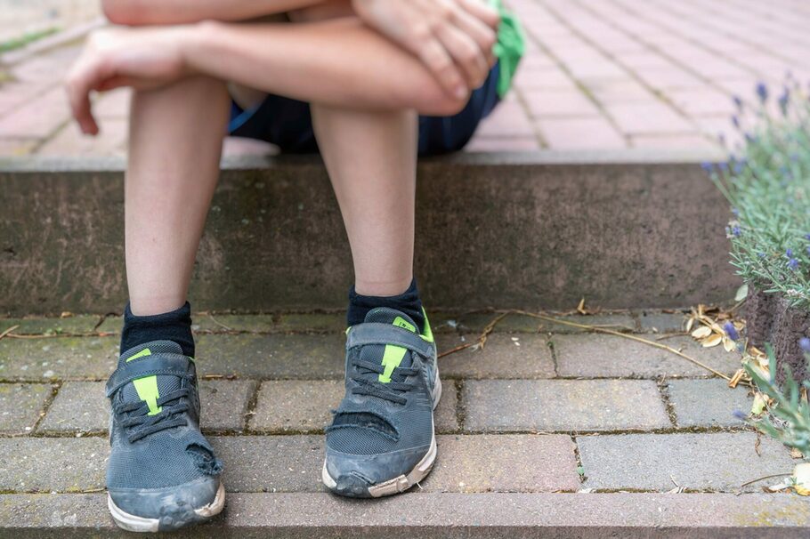 Little boy with broken shoes as a symbol of chSymbolbild Präventionskette gegen Kinderarmutild poverty