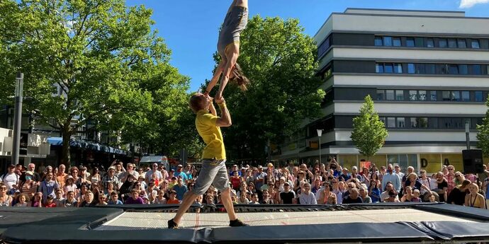 Ein Mann und eine Frau machen auf einem Trampolin umringt von Zuschauern akrobatische Aktionen.