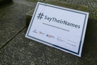 Ein Schild mit der Aufschrift "say their Names" vor dem Rathaus