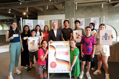 Eine Gruppe Kinder und zwei Erwachsene stehen neben einem Plakat zur Ausstellung „GG20 – die Grundrechte sind der Rede wert!“.