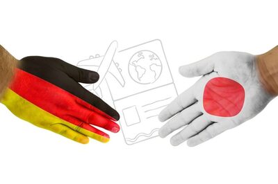 Zwei Hände in deutscher und japanischer Flagge bemalt zeigen auf ein Flugticket.