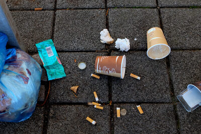 Eine Mülltüte, Zigarettenstummel, leere Kaffeebecher und Plastik liegen auf dem Boden.