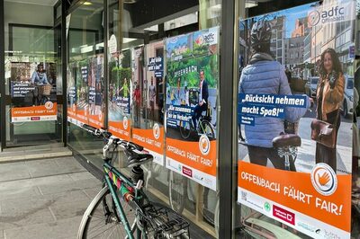 Plakate hängen in einem Schaufenster, davor steht ein Fahrrad.