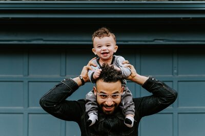 Ein junger Vater trägt lachend seinen Sohn auf den Schultern