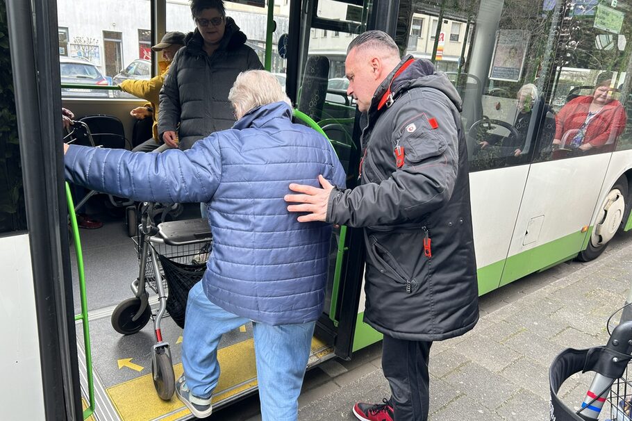 Coach Suat Öztürk hilft einer älteren Dame mit Rollator dabei, in einen Bus einzusteigen.