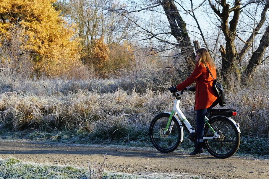 Eine Frau fährt mit einem Pedelec an Büschen mit Reif vorbei.