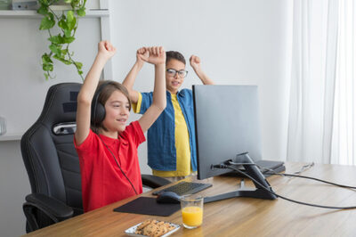 Zwei Jungen sitzen vorm Computer, strecken in Hände in Luft und sind stolz