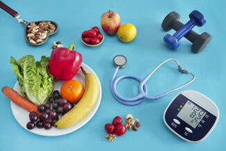 Obst, Gemüse, Nüsse, Hanteln, ein Stethoskop und ein Blutdruckmessgerät liegen auf einem Tisch.