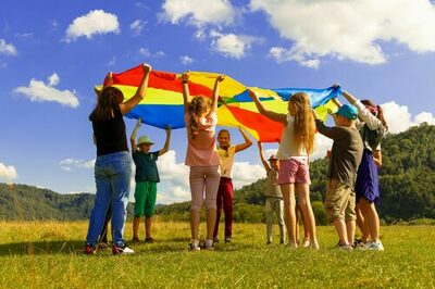 Kinder stehen auf einer Wiese und halten ein Tuch in Regenbogenfarben