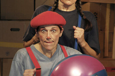 Man sieht de beiden Schauspielerinnen mit roter und blauer Mütze, Latzhosen und einem Ball.