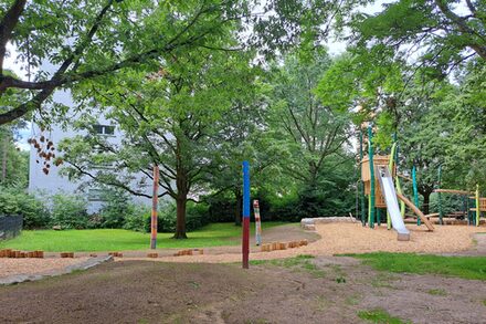 Zu sehen ist ein Spielplatz mit Klettergerüst, Rutsche und Bäumen im Hintergrund.