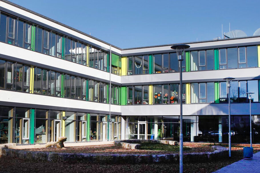 Das Schulgebäude in unterschiedlichen Grün- und Gelbtönen.